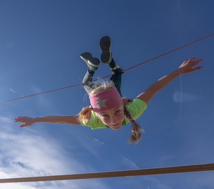 Dieses Bild zeigt ein Mädchen, dass kopfüber auf einem Seil im Slackline-Park auf der Schlossalmbahn hängt