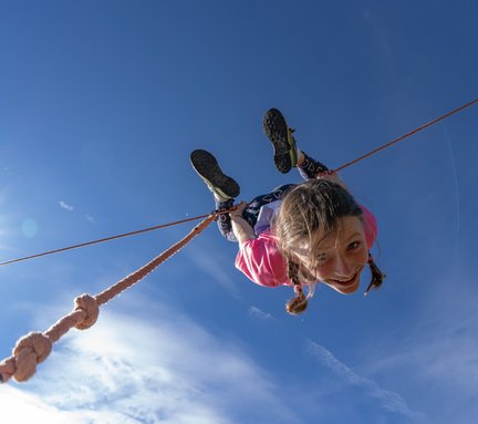 Dieses Bild zeigt ein Mädchen, dass kopfüber auf einem Seil im Slackline-park auf der Schlossalm hängt