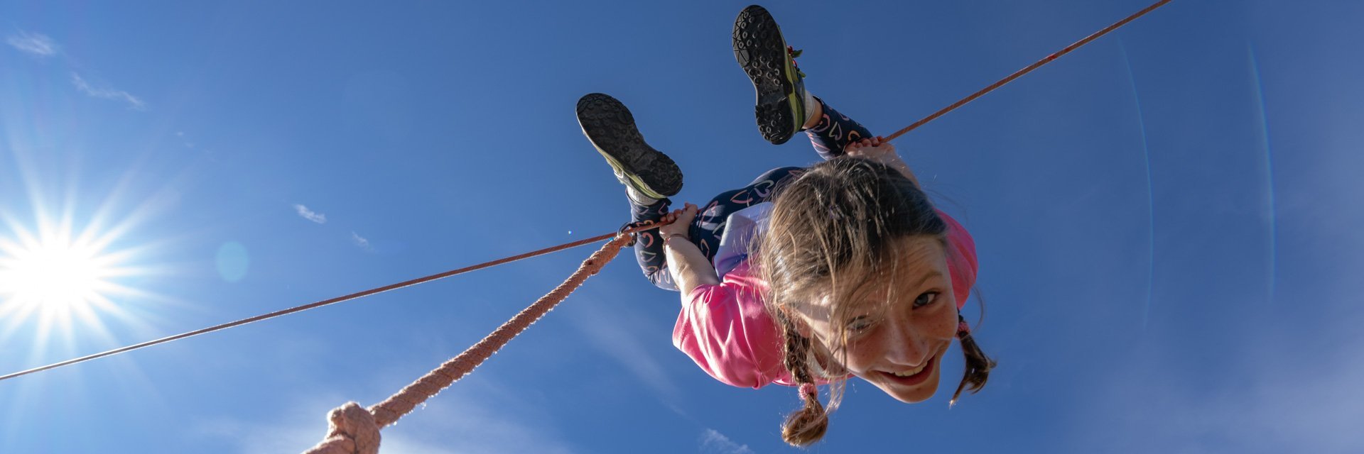 Dieses Bild zeigt ein Mädchen, dass kopfüber auf einem Seil im Slackline-park auf der Schlossalm hängt