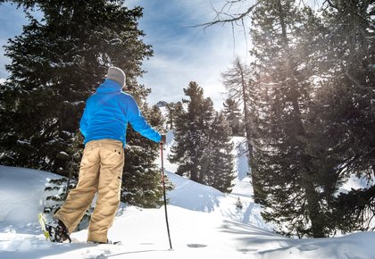 Schneeschuhwanderer stapft durch den verschneiten Wald am Graukogel