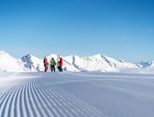 Dorfgastein-Großarltal Dieses Bild zeigt drei Skifahrer, die auf einer präparierten Piste in Gastein stehen