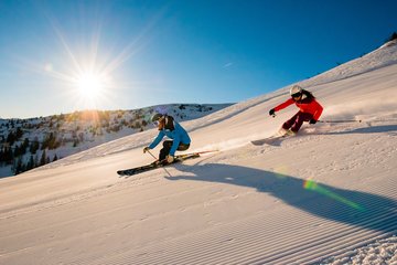 2 Skifahrer bei Sonnenaufgang auf der Piste in Dorfgastein
