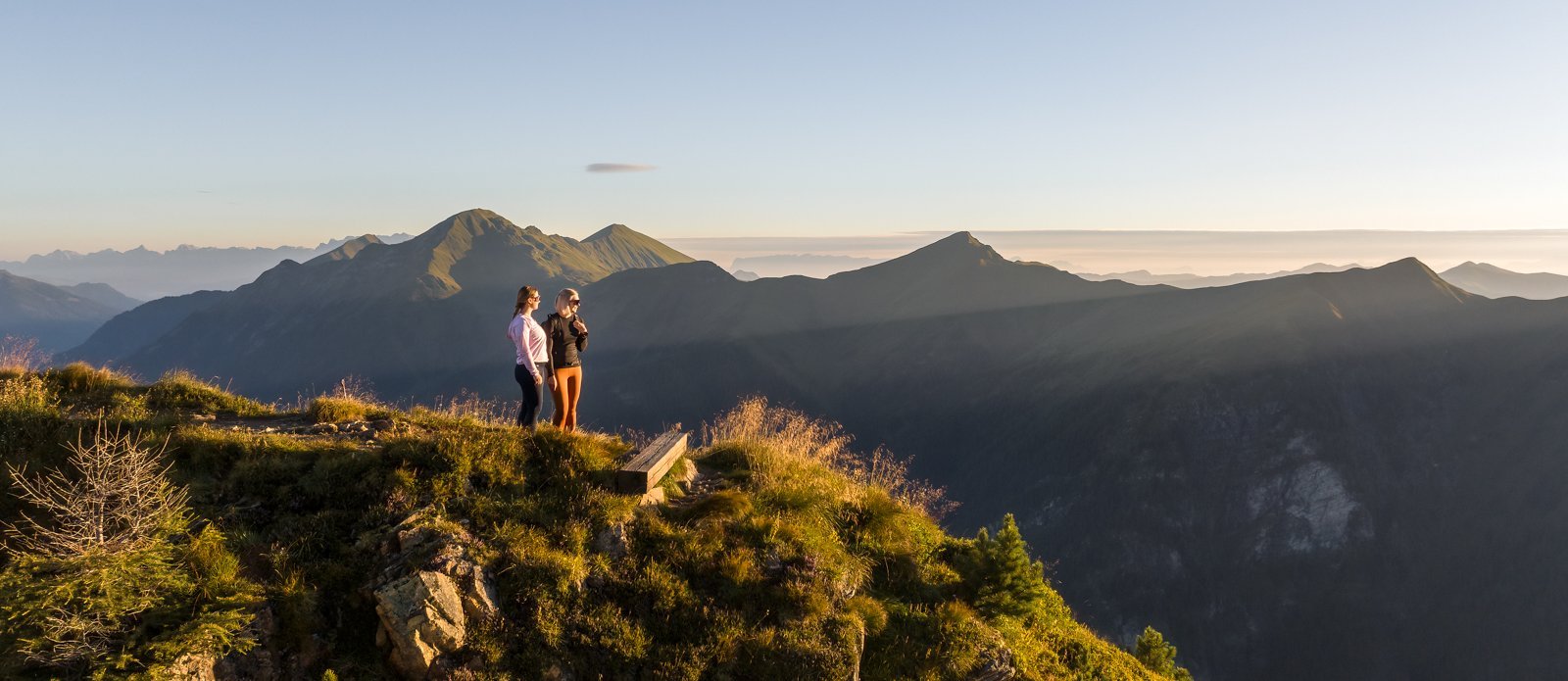 Dieses Bild zeigt zwei Frauen, die auf dem Graukogel stehen und das Bergpanorama bei Abend genießen. 