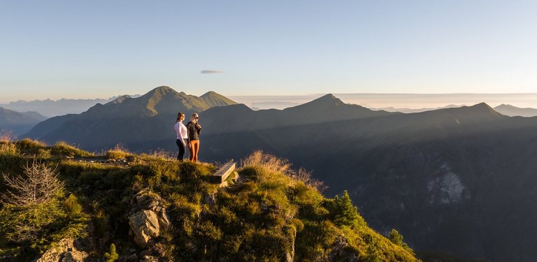 Dieses Bild zeigt zwei Frauen, die auf dem Graukogel stehen und das Bergpanorama bei Abend genießen. 