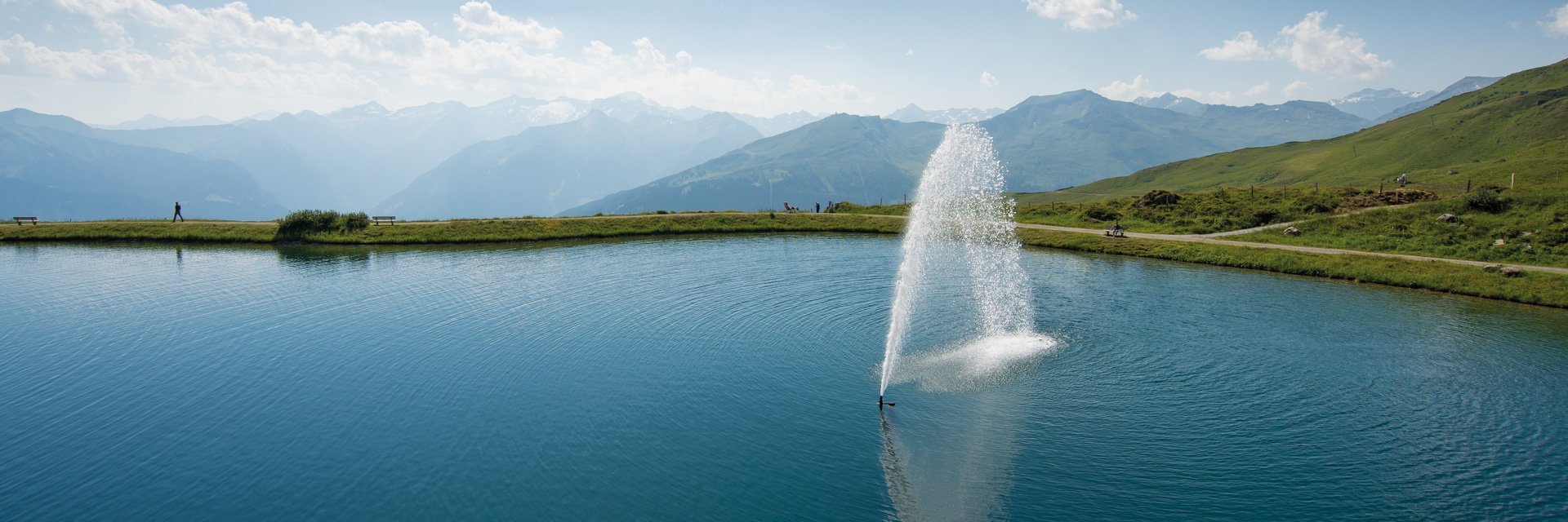 Dieses Bild zeigt den Schlossalmsee mit einer Wasserfontäne in der Mitte