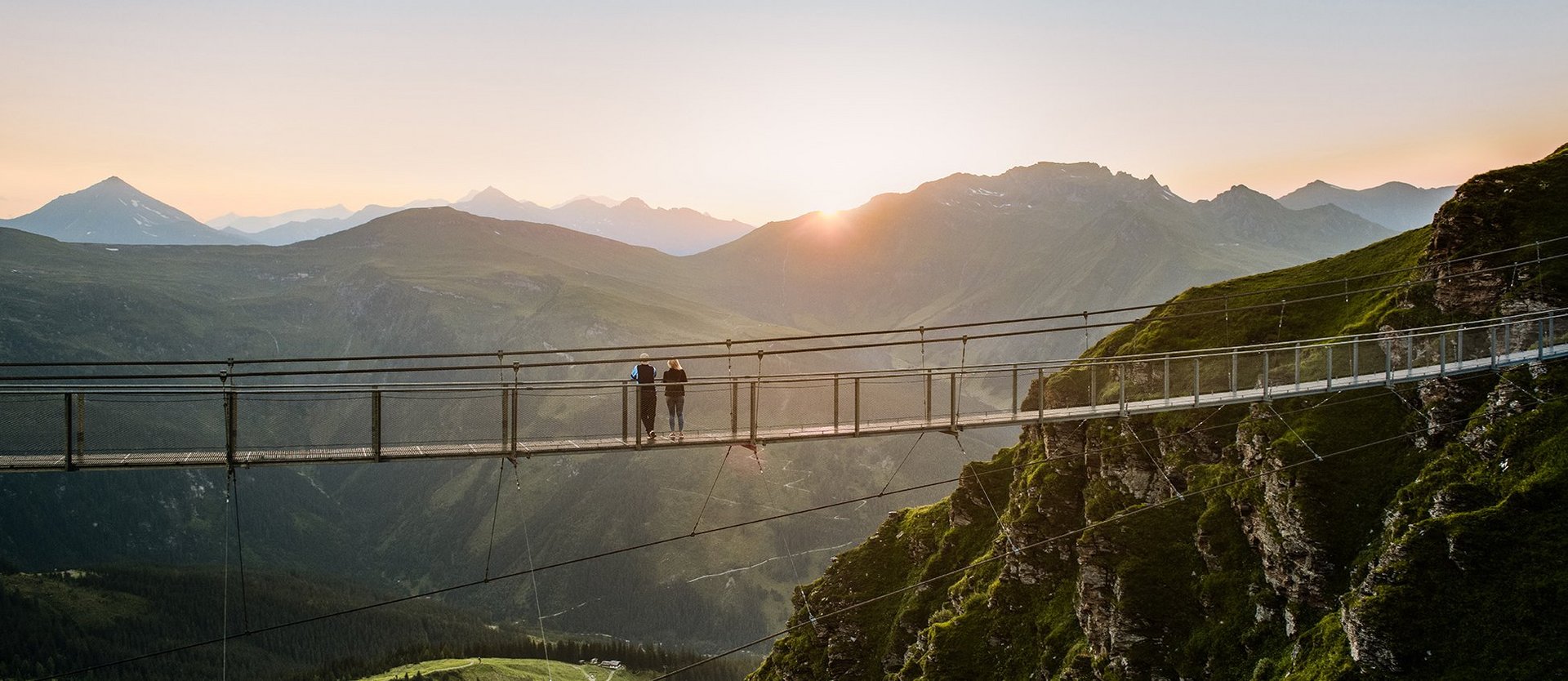 Dieses Bild zeigt die Hängebrücke am Stubnerkogel im Sommer mit zwei Menschen bei Sonnenuntergang