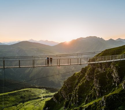 Dieses Bild zeigt die Hängebrücke am Stubnerkogel im Sommer mit zwei Menschen bei Sonnenuntergang