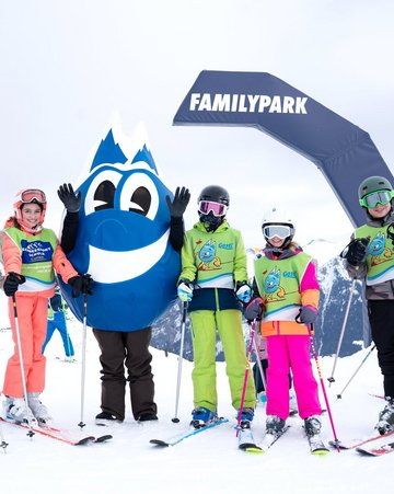 Dieses Bild zeigt eine Gruppe von Skischülern mit dem Maskottchen Gasti vor dem Familypark in Gastein