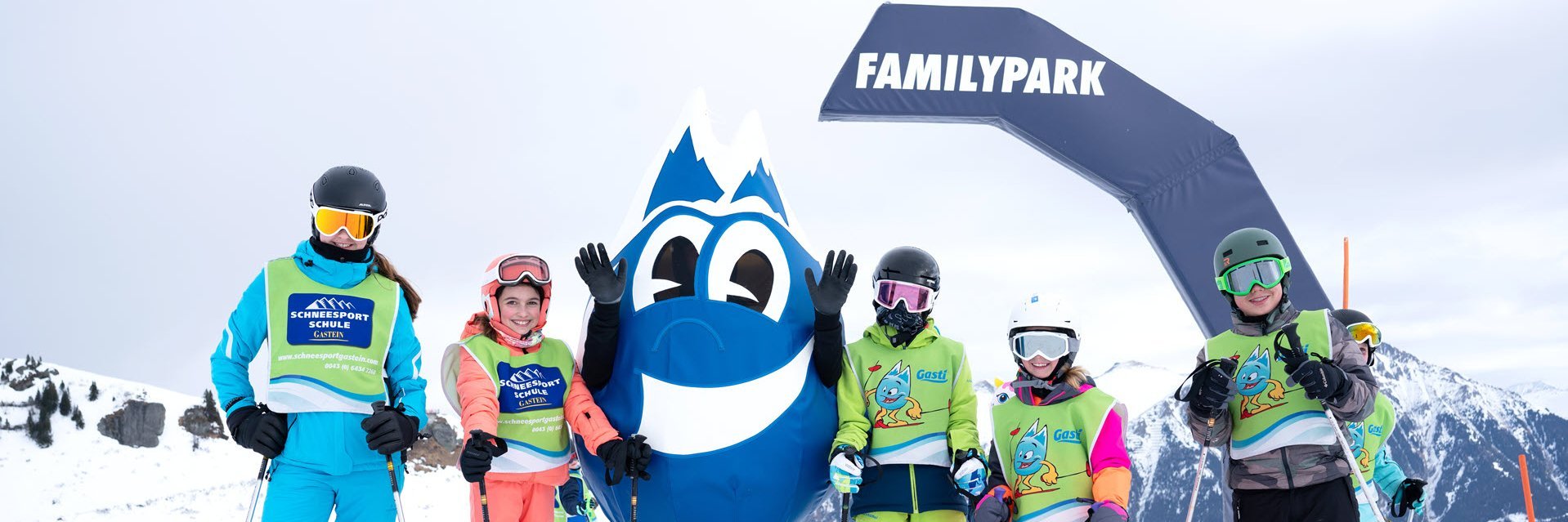 Dieses Bild zeigt eine Gruppe von Skischülern mit dem Maskottchen Gasti vor dem Familypark in Gastein