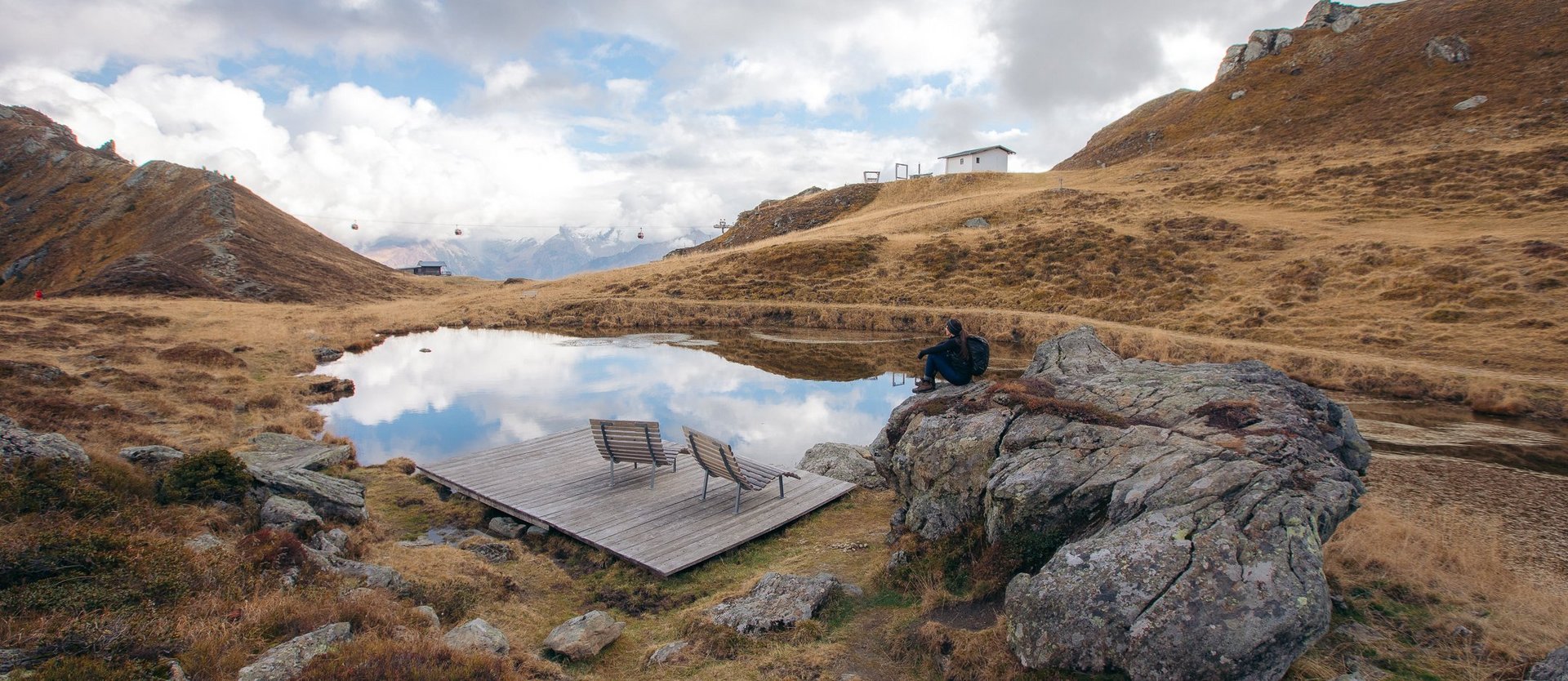 Dieses Bild zeigt eine Wanderin im Herbst, die auf einem Felsen neben einem See auf der Schlossalm sitzt und in die Ferne sieht