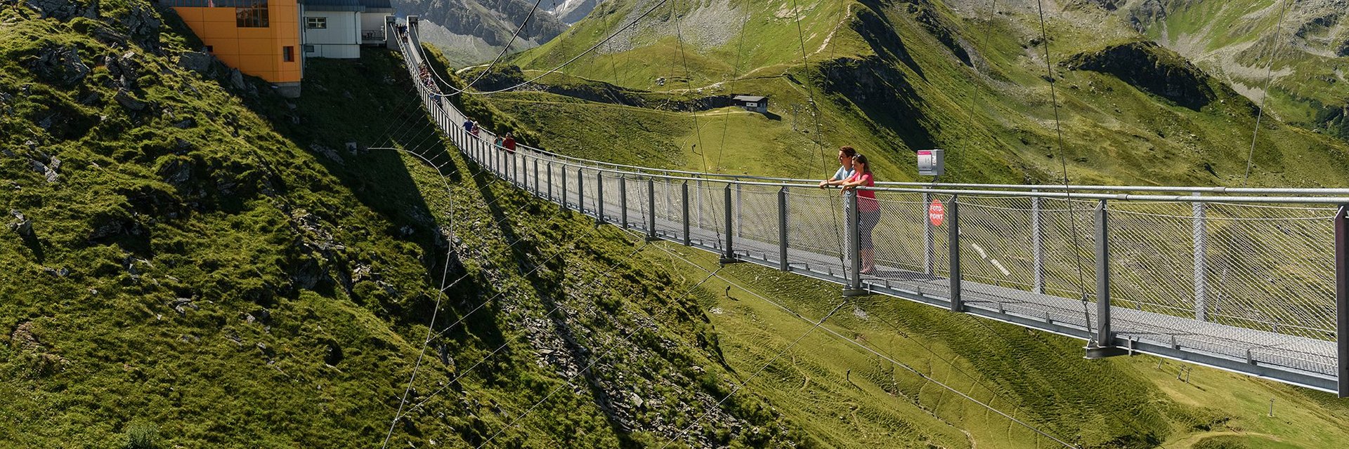 Die Hängebrücke am Stubnerkogel im Sommer, auf der zwei Personen in die Ferne blicken. In der Distanz sind weitere Personen zu erkennen.
