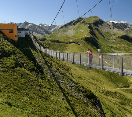 Die Hängebrücke am Stubnerkogel im Sommer, auf der zwei Personen in die Ferne blicken. In der Distanz sind weitere Personen zu erkennen.