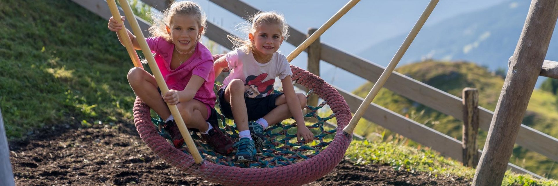 Dieses Bild zeigt zwei Mädchen, die in einer Nestschaukel in einem Gasteiner Spielplatz schaukeln