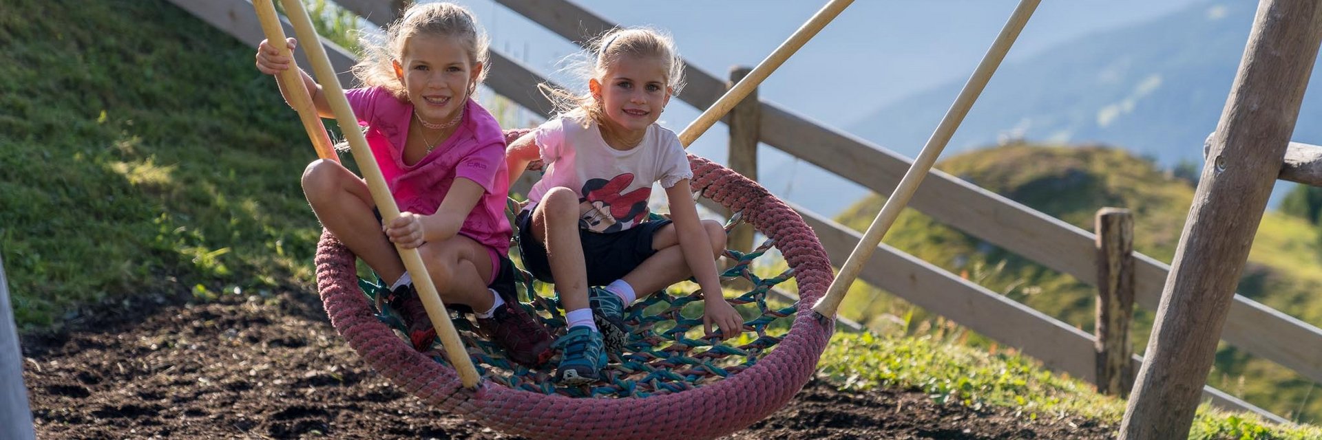 Dieses Bild zeigt zwei Mädchen, die in einer Nestschaukel in einem Gasteiner Spielplatz schaukeln
