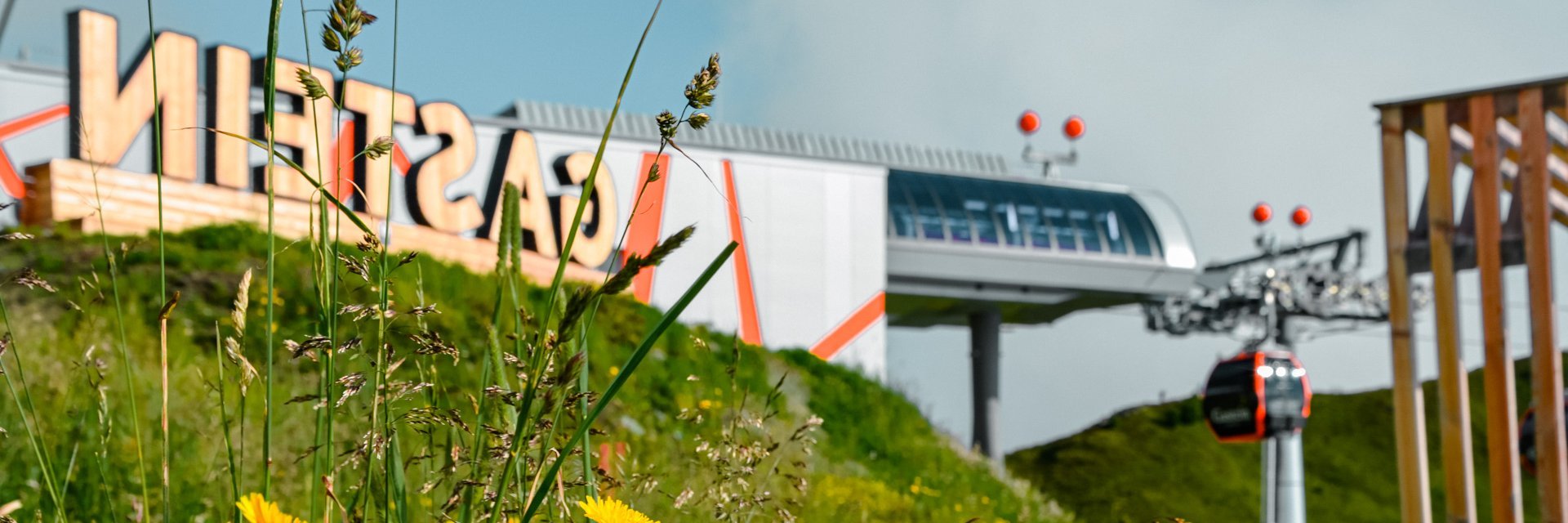 Dieses Bild zeigt die Bergstation Schlossalm, das Gasteinschild und eine Sommerliche Blumenwiese